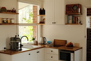 Una cocina con cafetera, hervidor y frutero sobre la encimera.