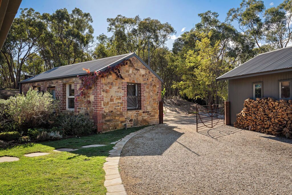 A stone building with a sloped roof, surrounded by a gravel driveway and a small garden area with a pathway leading to the entrance.