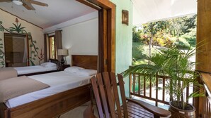 Une chambre avec deux lits, un ventilateur de plafond, une chaise en bois et un balcon agrémenté d’un pot de fleurs.