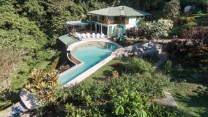 Une maison à deux étages avec une piscine, entourée d’une végétation luxuriante.