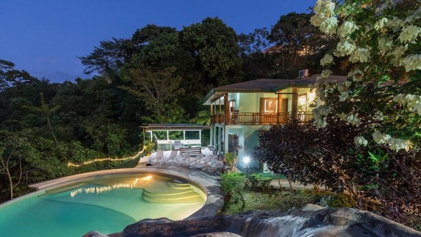 Une maison avec une piscine, entourée d’arbres et d’une cascade.