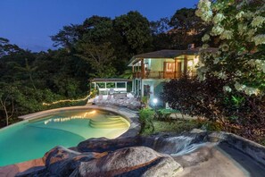 Una casa circondata da alberi e una cascata, con una piscina.