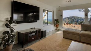 Un salon doté d’un grand téléviseur, d’un canapé, d’une table basse et offrant une vue sur un paysage montagneux grâce à de grandes fenêtres.