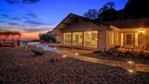 Une maison moderne dotée de grandes fenêtres en verre, d’un chemin en pierre et d’un espace extérieur bien éclairé au crépuscule.