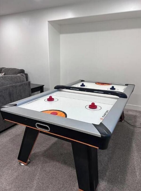 A foosball table in a room with a grey carpet and a grey couch.