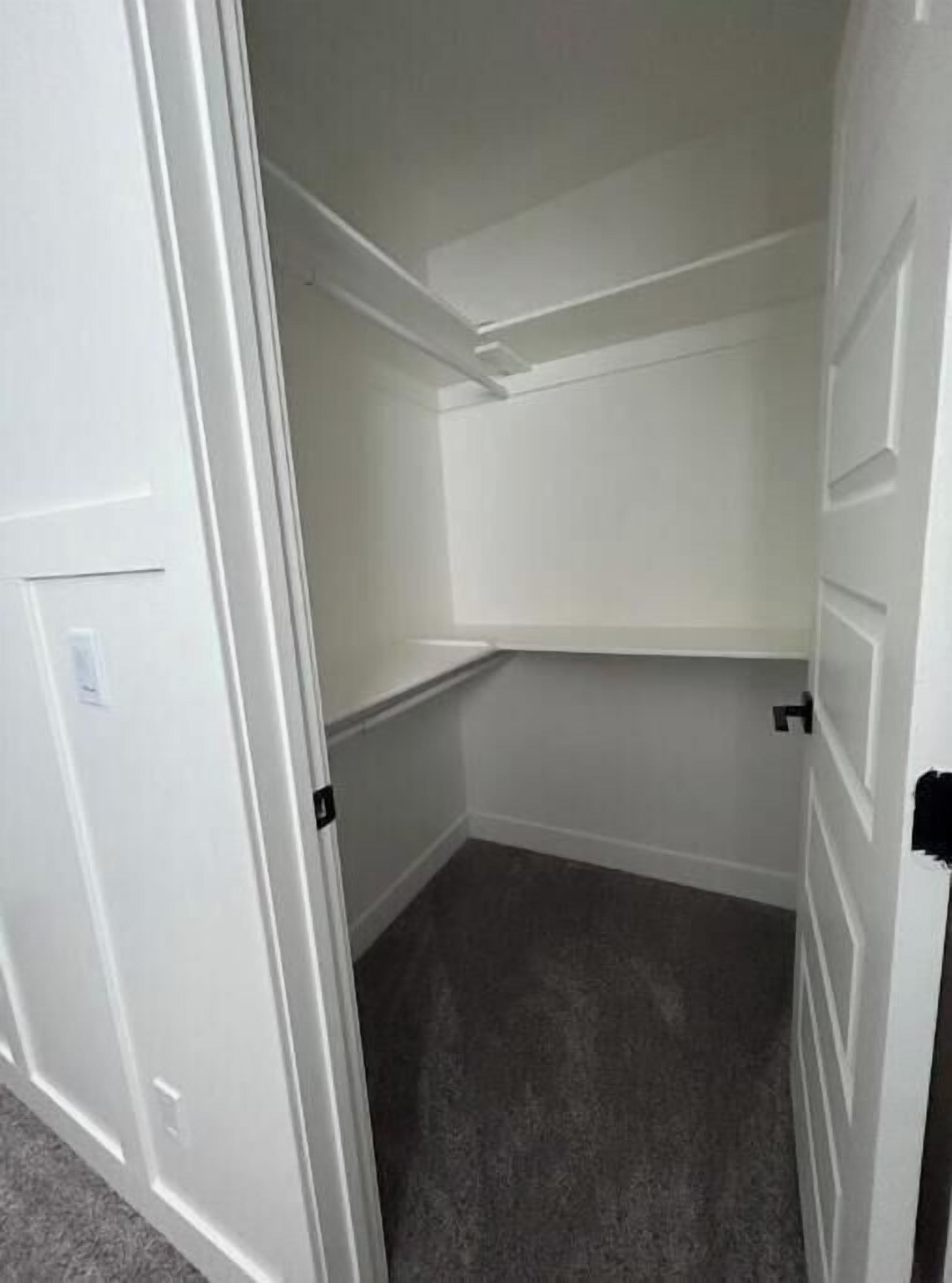 A small, empty room with white walls and a grey carpet.