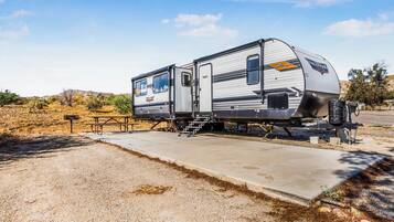 A recreational vehicle (RV) parked on a gravel surface with a concrete ramp leading to a picnic table and a small building.