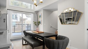 A modern kitchen with a dining area, a large window, and a geometric mirror on the wall.