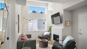 A modern living room with a fireplace, a sofa, a chair, and a television mounted on the wall.
