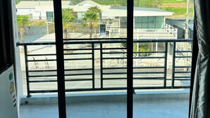 A room with large sliding glass doors leading to a balcony with a metal railing, a view of buildings and greenery outside. - Langmoresort (Ongkharak)