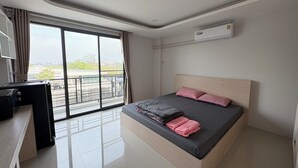 A modern bedroom with a large bed, a desk, and a view through a sliding door to the outside. - Langmoresort (Ongkharak)