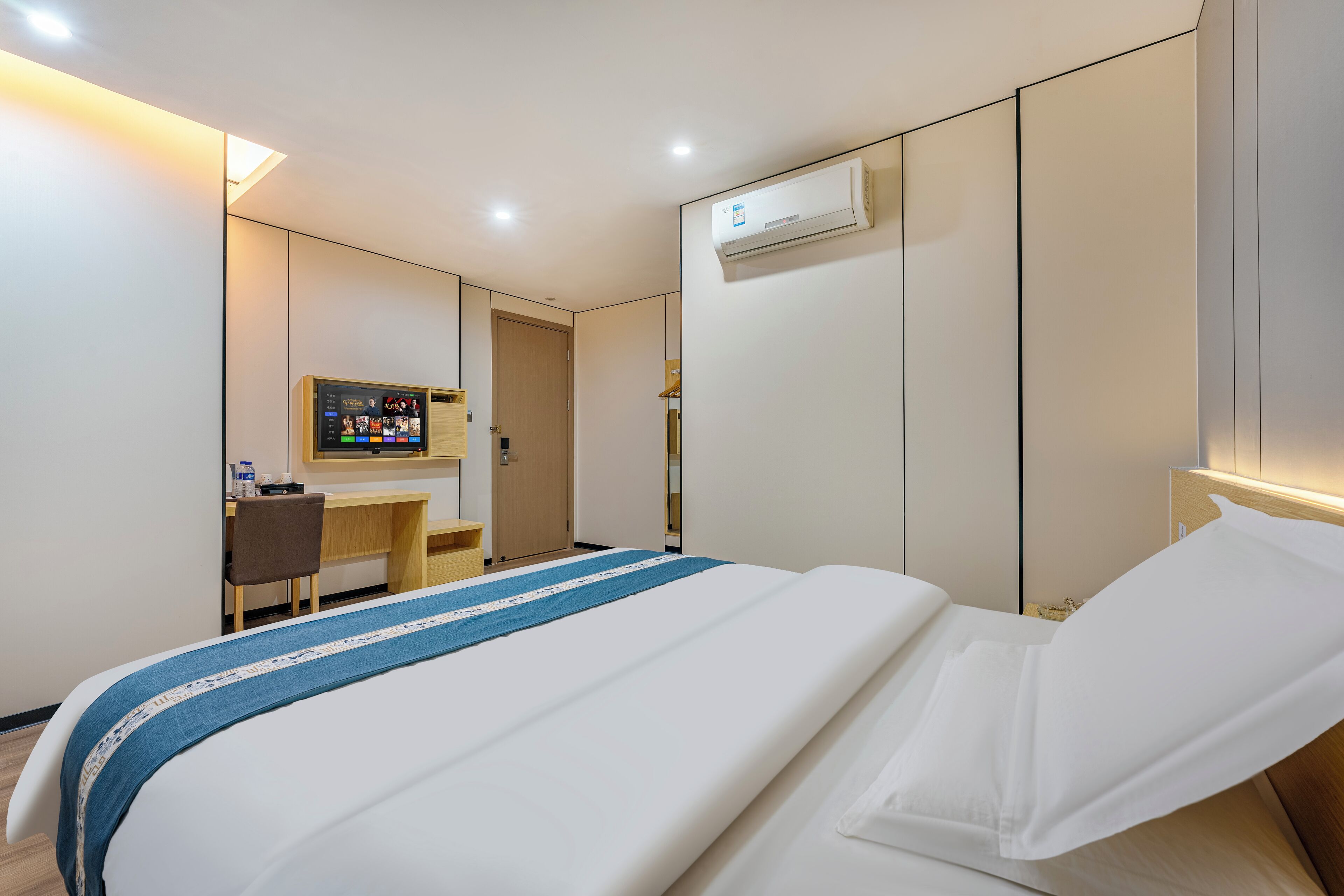 Ein Hotelzimmer mit Bett, Schreibtisch, Stuhl, Fernseher und Klimaanlage.