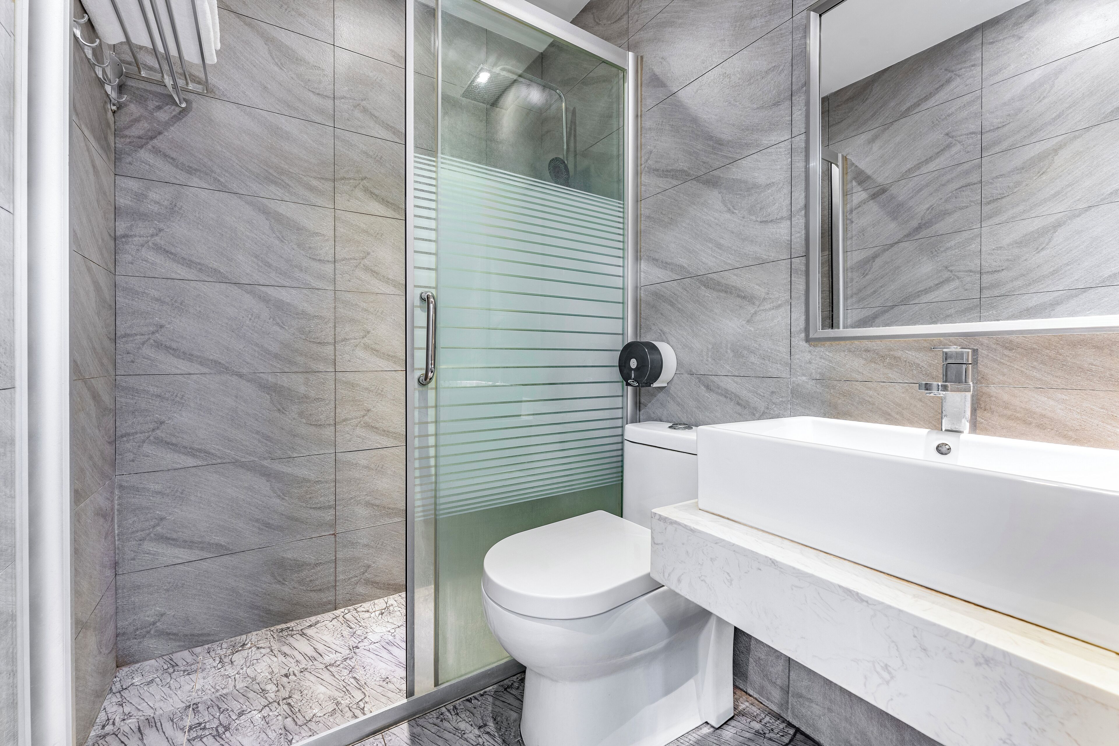 Une salle de bain moderne avec une douche à parois de verre, des toilettes blanches et un lavabo recouvert de carreaux de marbre.
