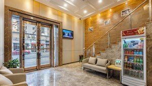 A lobby with a marble floor, a sofa, a refrigerator with beverages, a television, and a staircase. - Guangzhou Kaiyue Hotel Luoxi Subway Station Branch - Free Deliver Service to Canton Fair Complex During Canton Fair Period (Guangzhou)