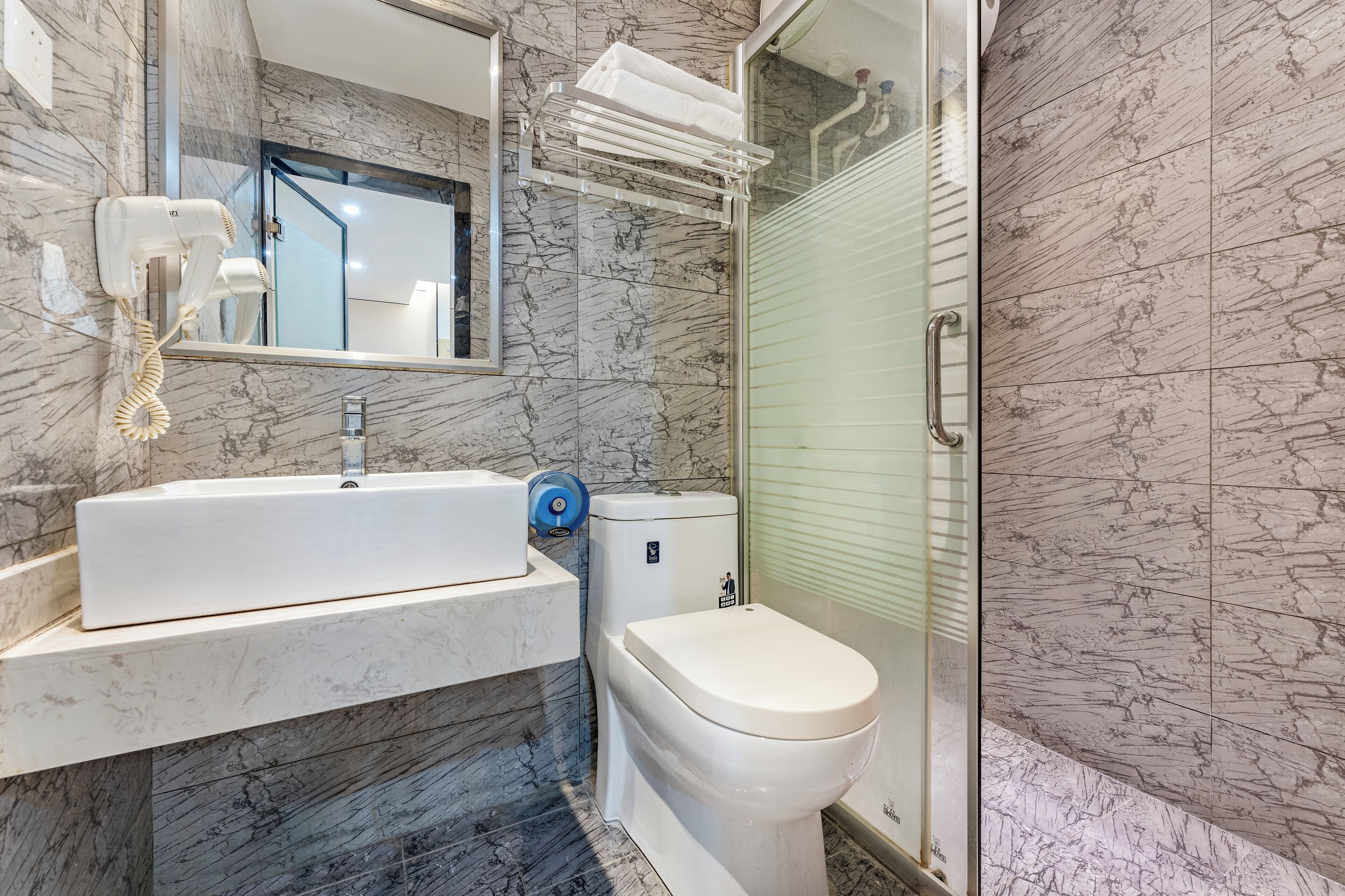 A bathroom with a marble sink, a toilet, a hairdryer, and a towel rack.