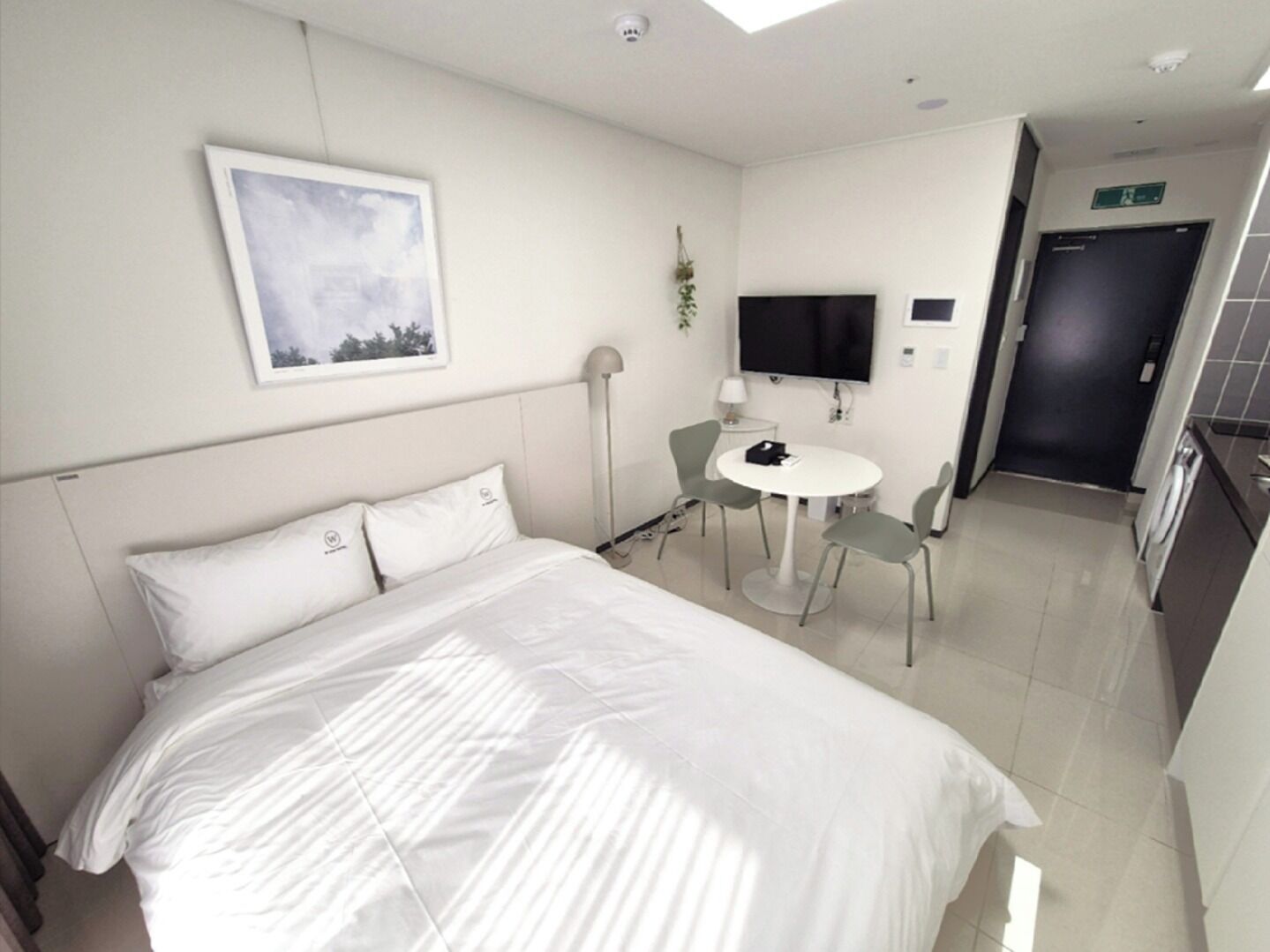 A hotel room with a bed, a desk with a chair, a TV, and a door.