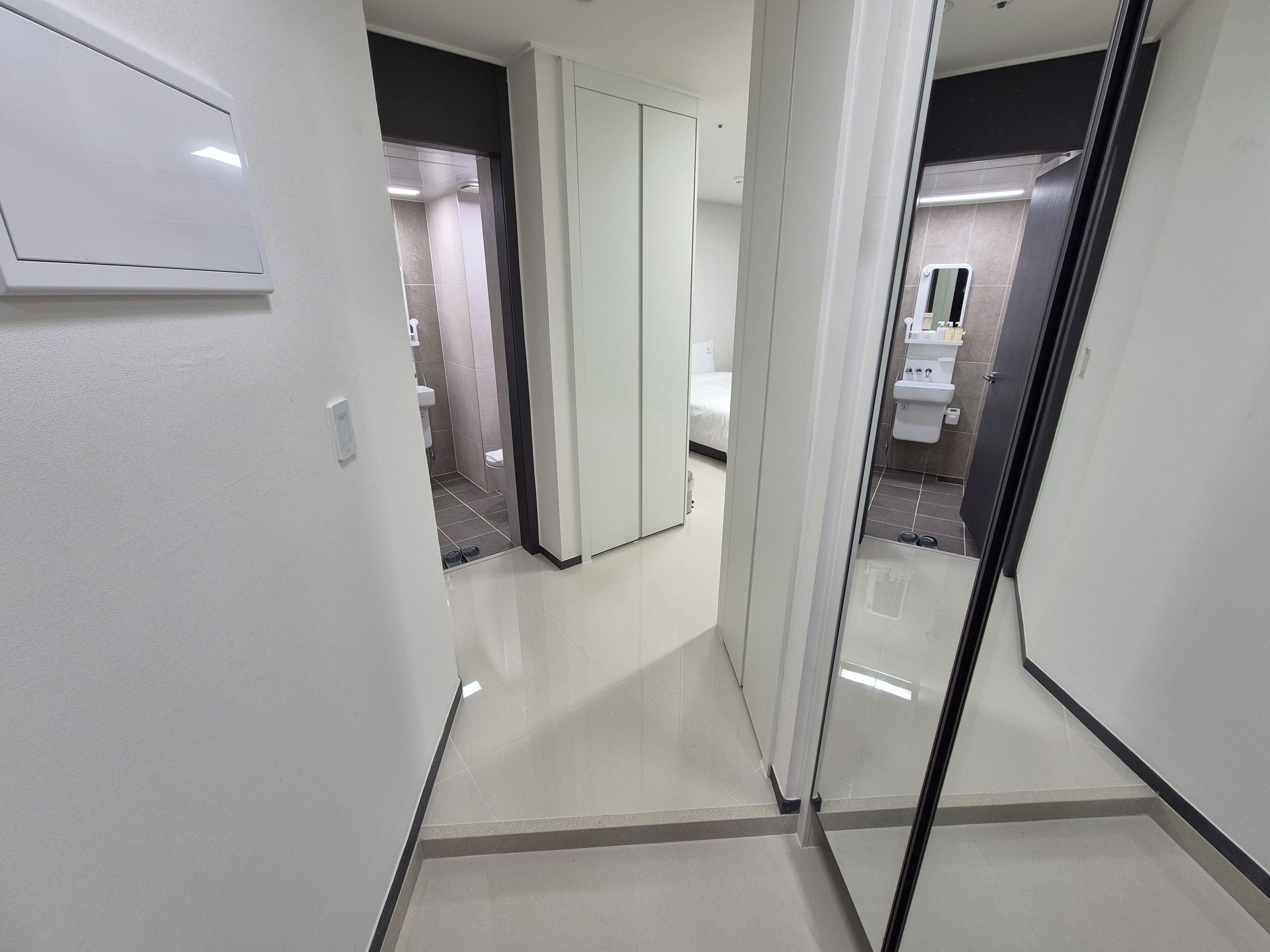A modern hotel corridor with a bathroom visible through a glass door, featuring a toilet, sink, and mirror.