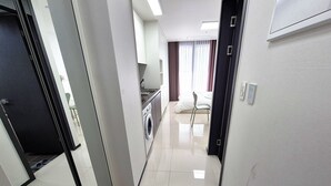 A hallway leading to a bedroom with a bed, a chair, and a washing machine. - W Stay Hotel Busan City Hall (Busan)