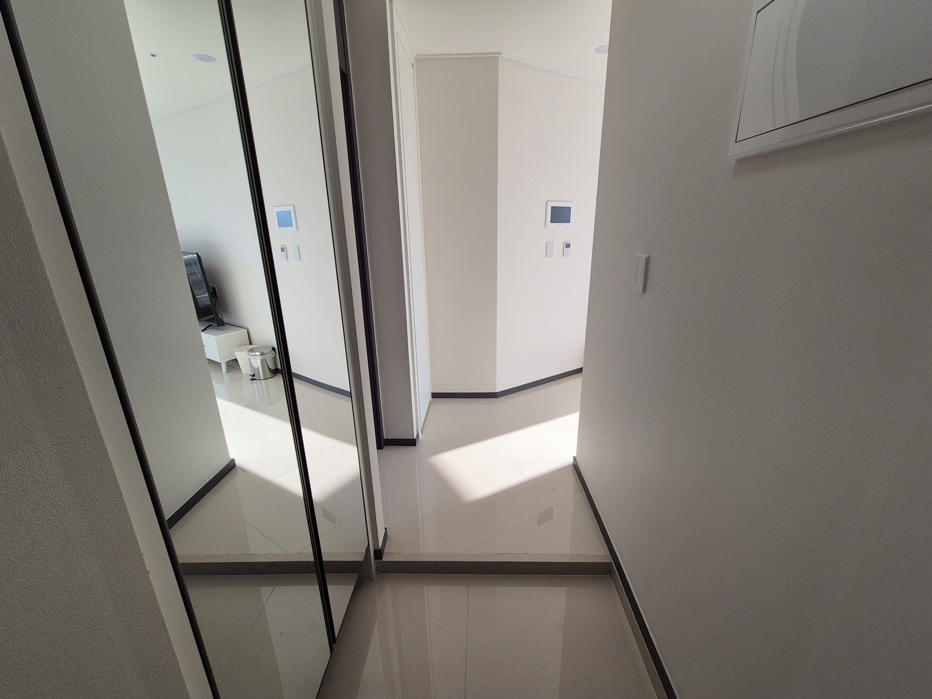 A corridor with a glass partition, a door at the end, and a small bathroom with a toilet and sink.