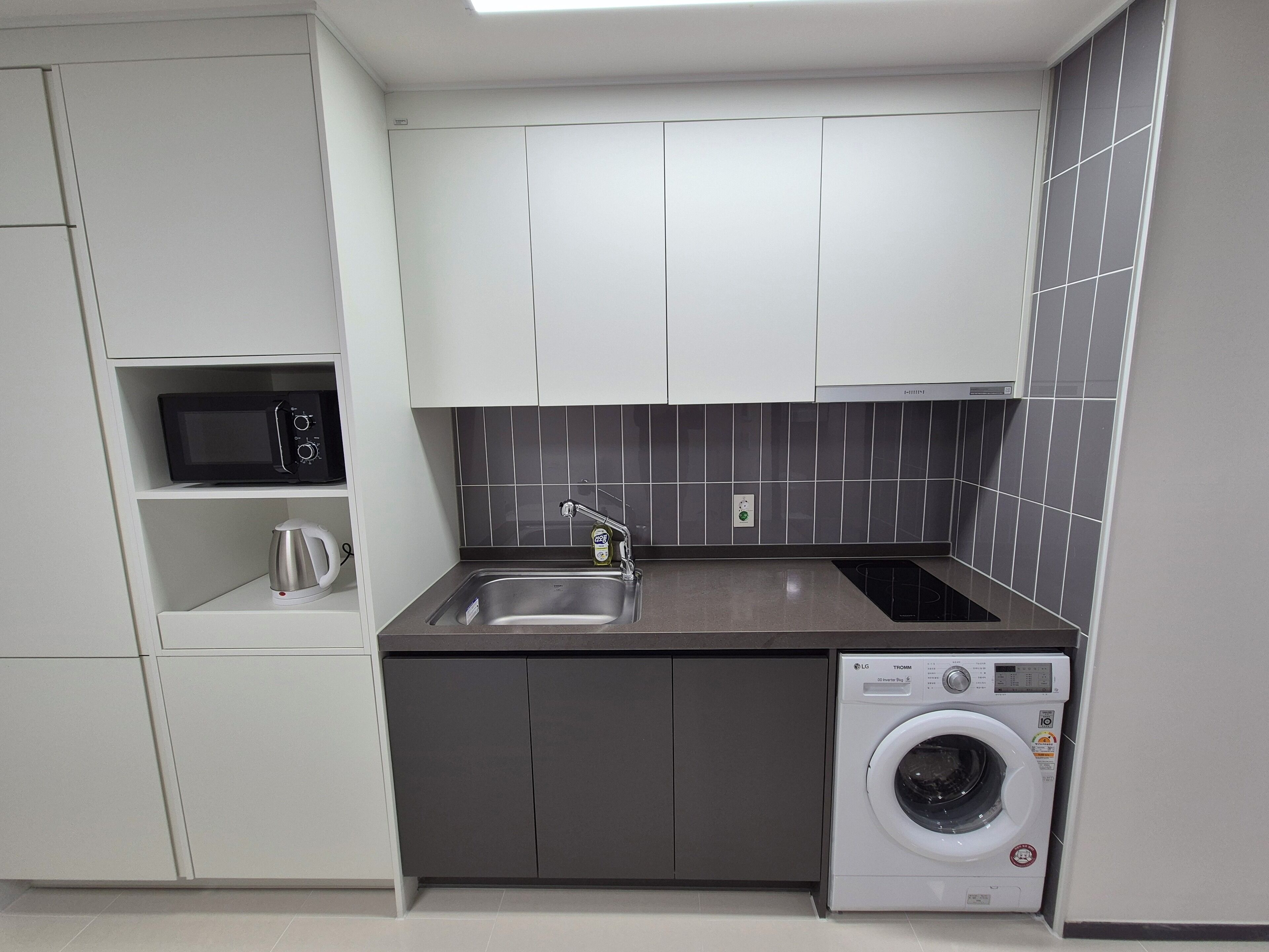 Cocina compacta con microondas, lavabo, hervidor y lavadora.
