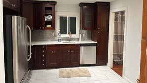 Cucina moderna con pensili in legno scuro, frigorifero in acciaio inossidabile, lavastoviglie e una finestra sopra il lavello.