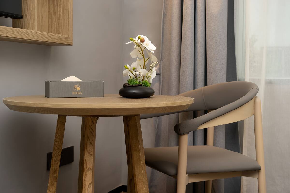 A wooden table with a vase of white flowers, a tissue box, and a chair.