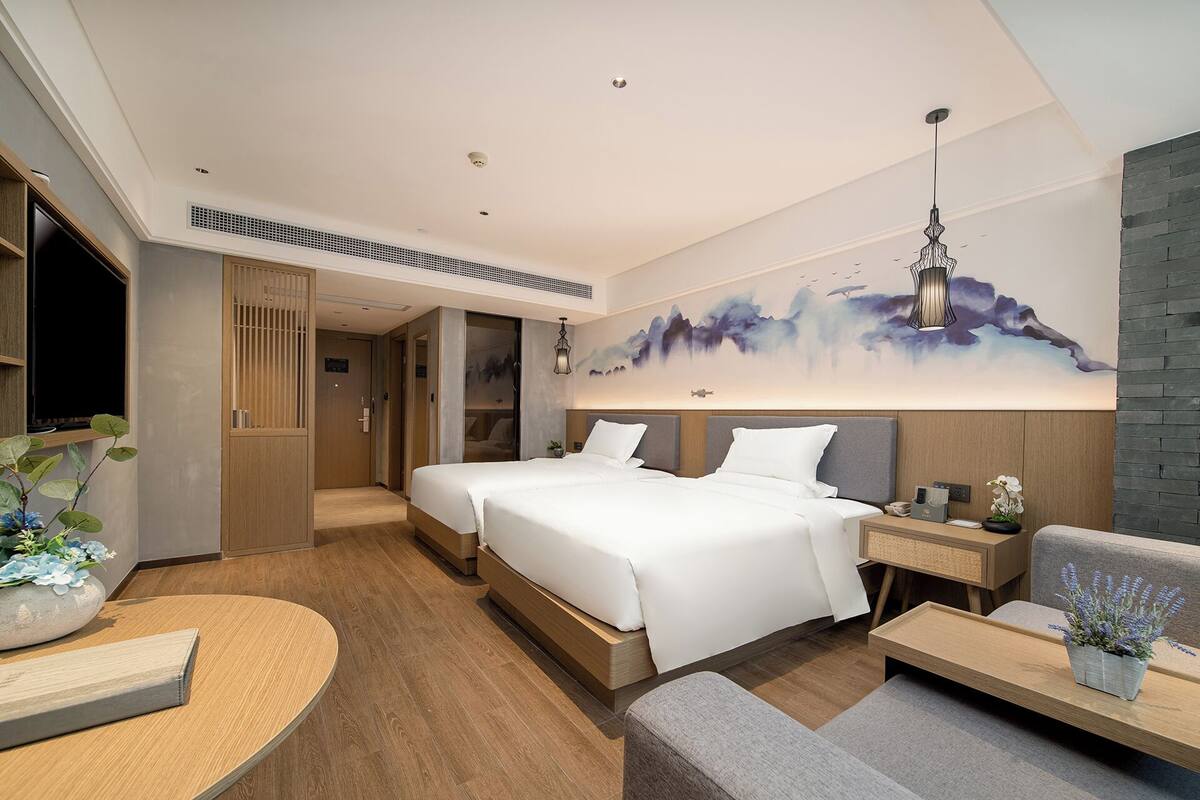 A modern hotel room with two beds, a seating area, and a large wall painting.