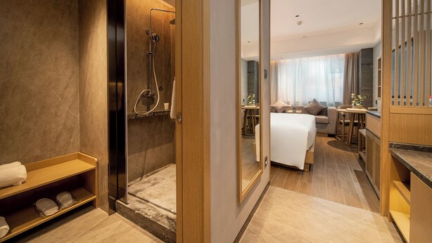 A modern hotel bathroom with a shower, a vanity, and a seating area with a sofa and table.