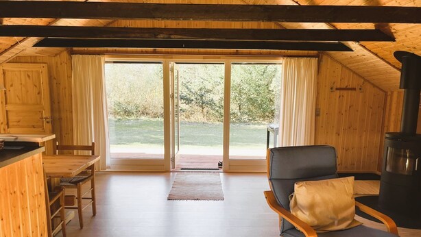 A wooden cabin interior with a dining table, a chair, a sofa, and a fireplace. - "Urban" - 140m from the sea by Interhome (Martofte)