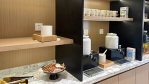 Estación de café con cafetera, tazas y un cuenco de nueces.