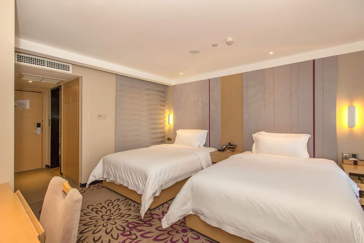 A hotel room with two beds, a desk, and a patterned carpet.
