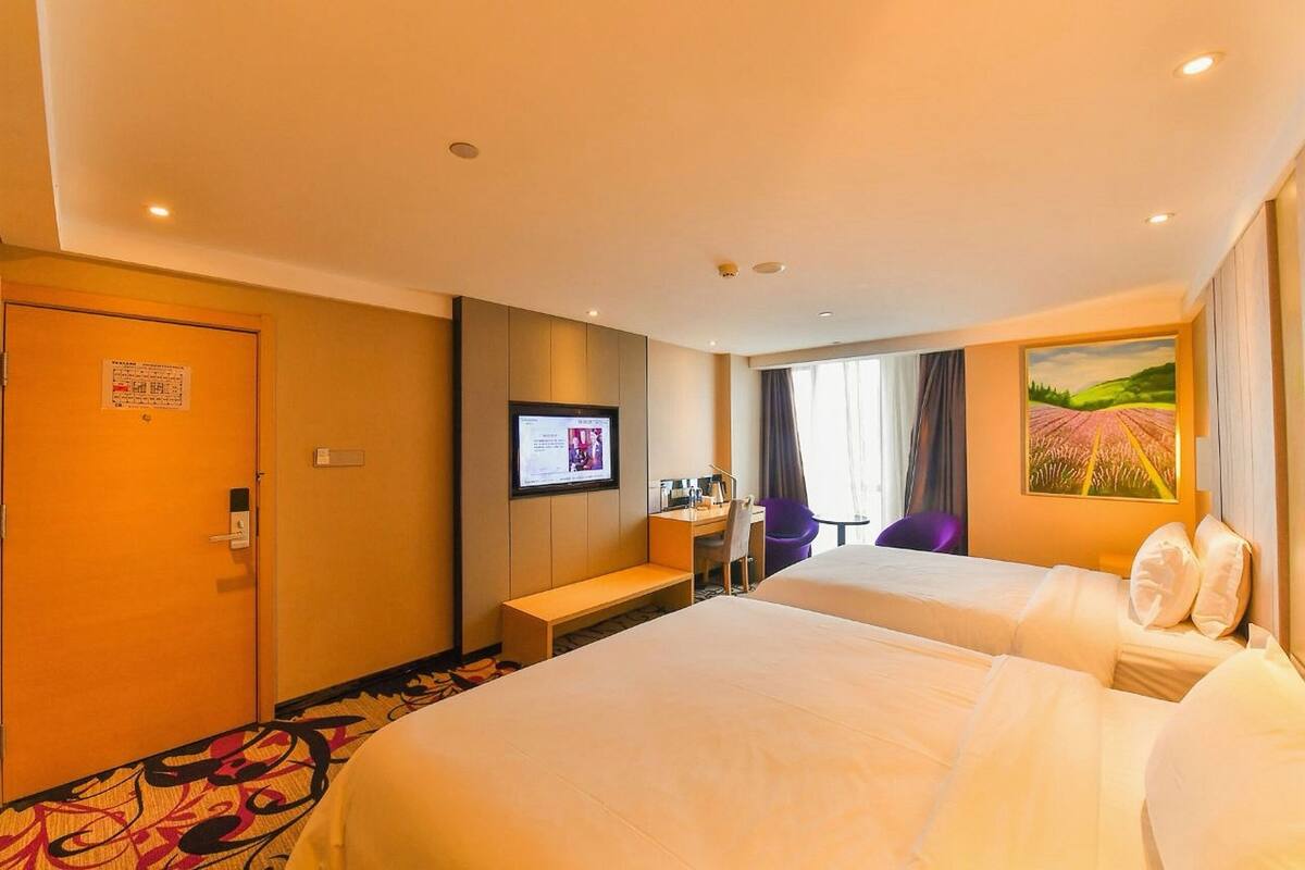 A hotel room with two beds, a desk, a TV, and a painting on the wall.