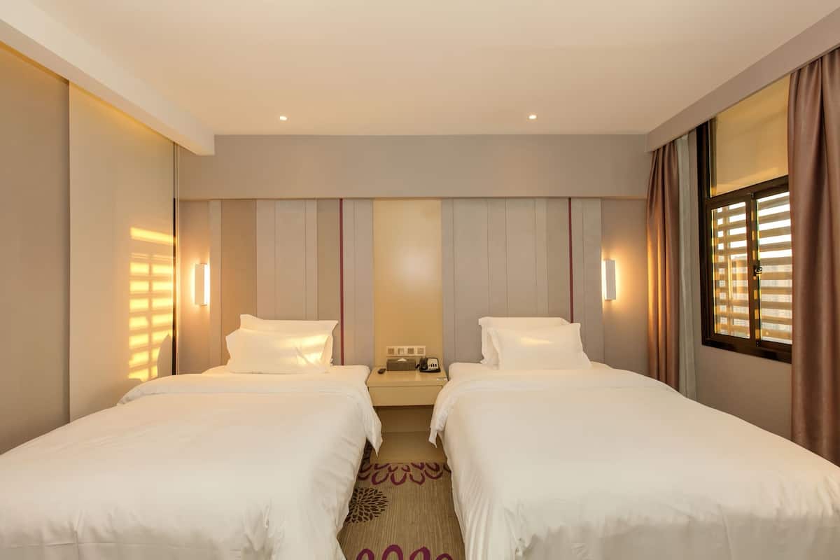 A hotel room with two beds, a nightstand, and a window with curtains.