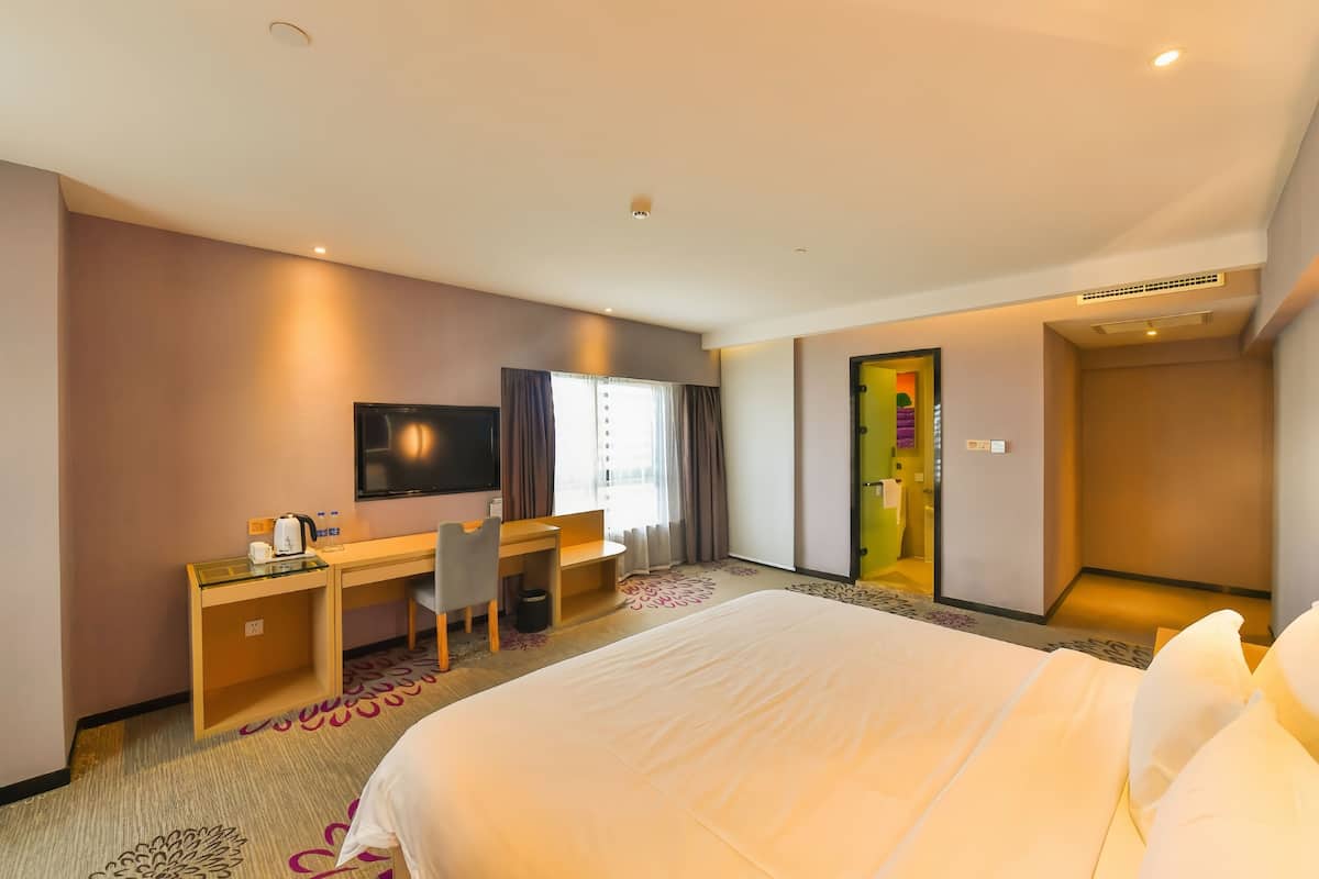 A hotel room with a bed, desk, chair, TV, and a door leading to another room.