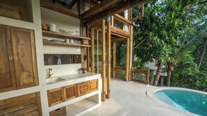 Une cuisine moderne avec des meubles en bois, un plan de travail blanc et une grande fenêtre donnant sur un espace piscine.