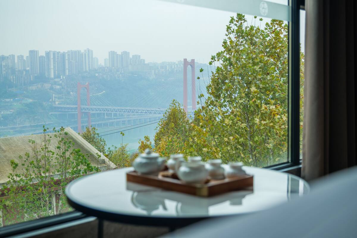 A table with teapots in a room with a view of a bridge and cityscape.