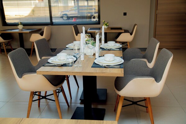 A dining area with a wooden table set for four, surrounded by grey upholstered chairs. - NEW AMAAN HOTEL (Zanzibar Town)
