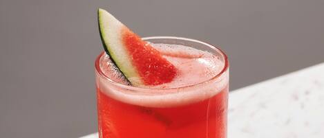 A tall glass with a red beverage, a slice of lime, and a straw on a marble surface.