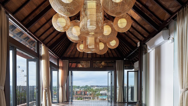 A spacious balcony with wooden flooring, large windows, and a view of buildings and greenery. - Aahana Village Bali  (Tibubeneng)