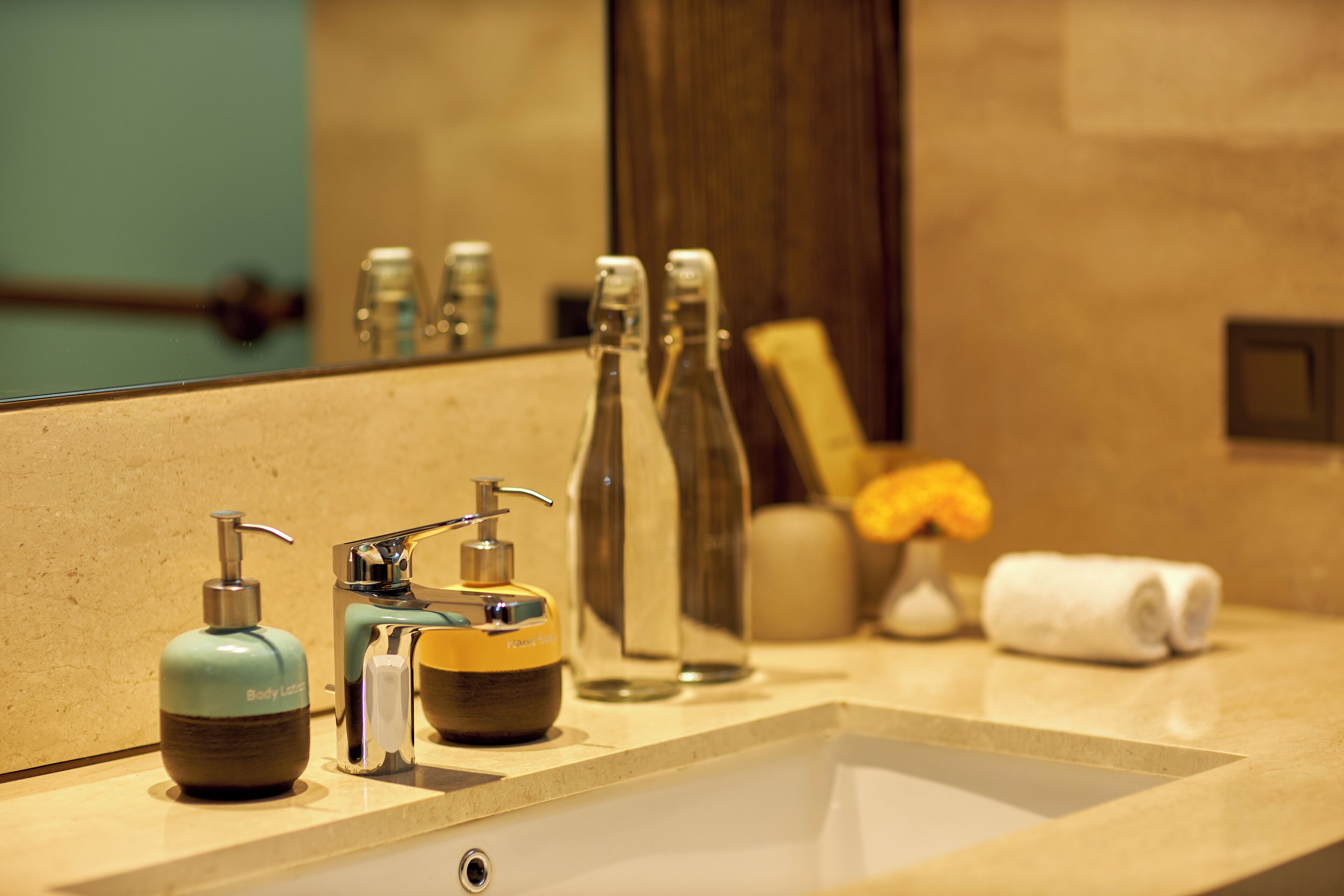 A bathroom sink with a mirror, a soap dispenser, a bottle, and a towel.