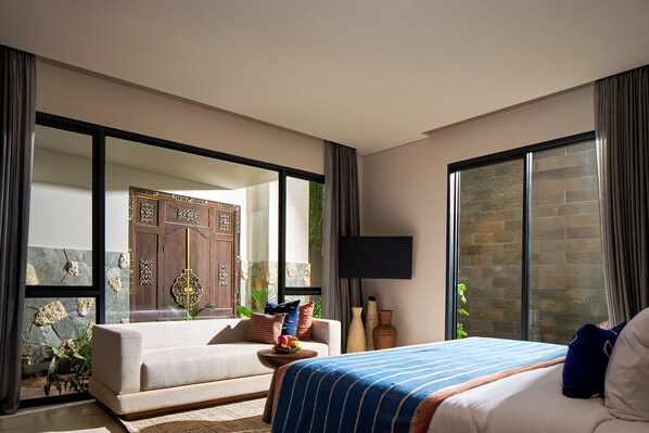 Ein modernes Hotelzimmer mit einem großen Bett, einer Couch, einem Fernseher und Blick ins Freie.
