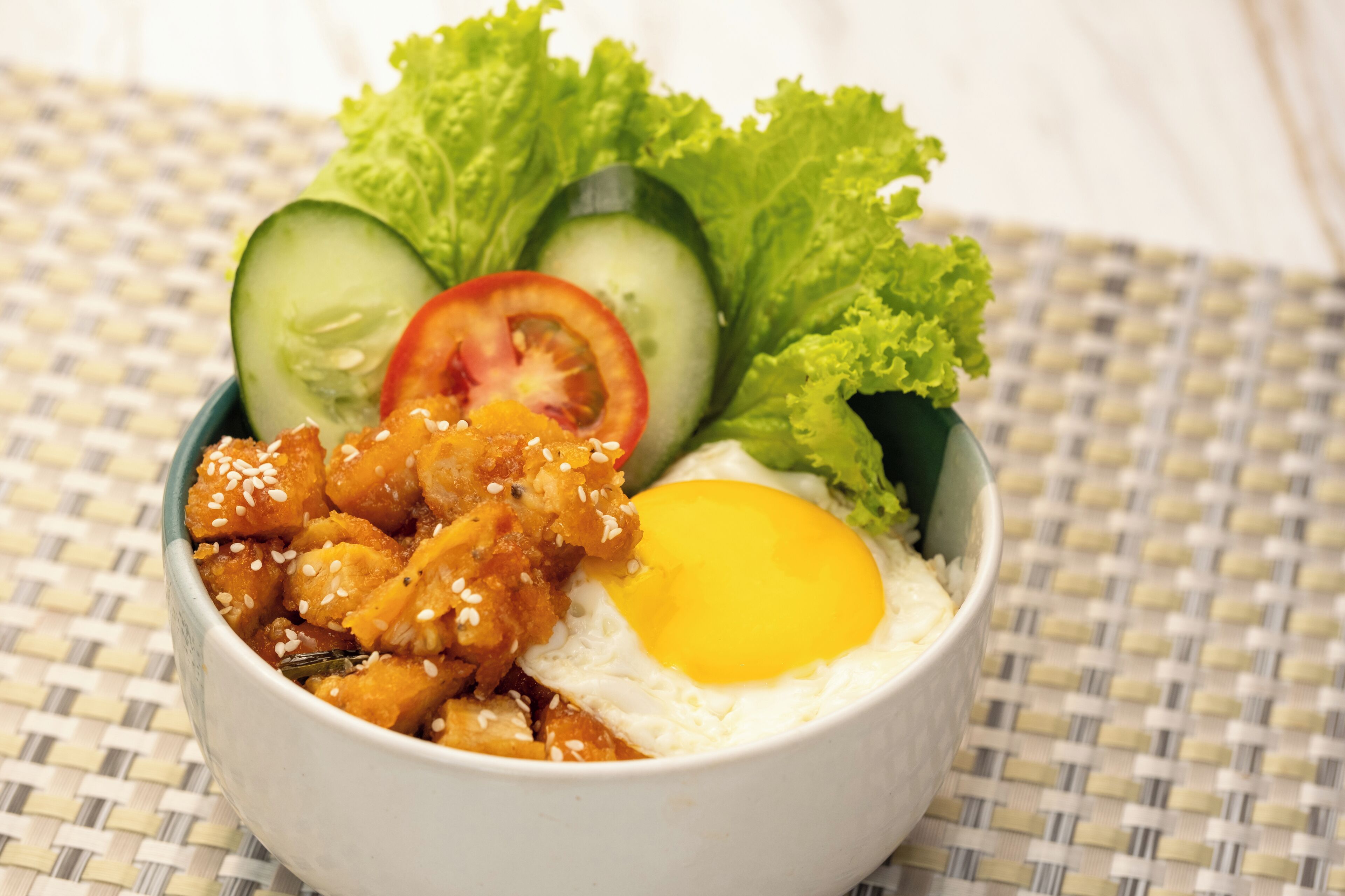 A bowl of food with a fried egg, sesame seeds, and vegetables.
