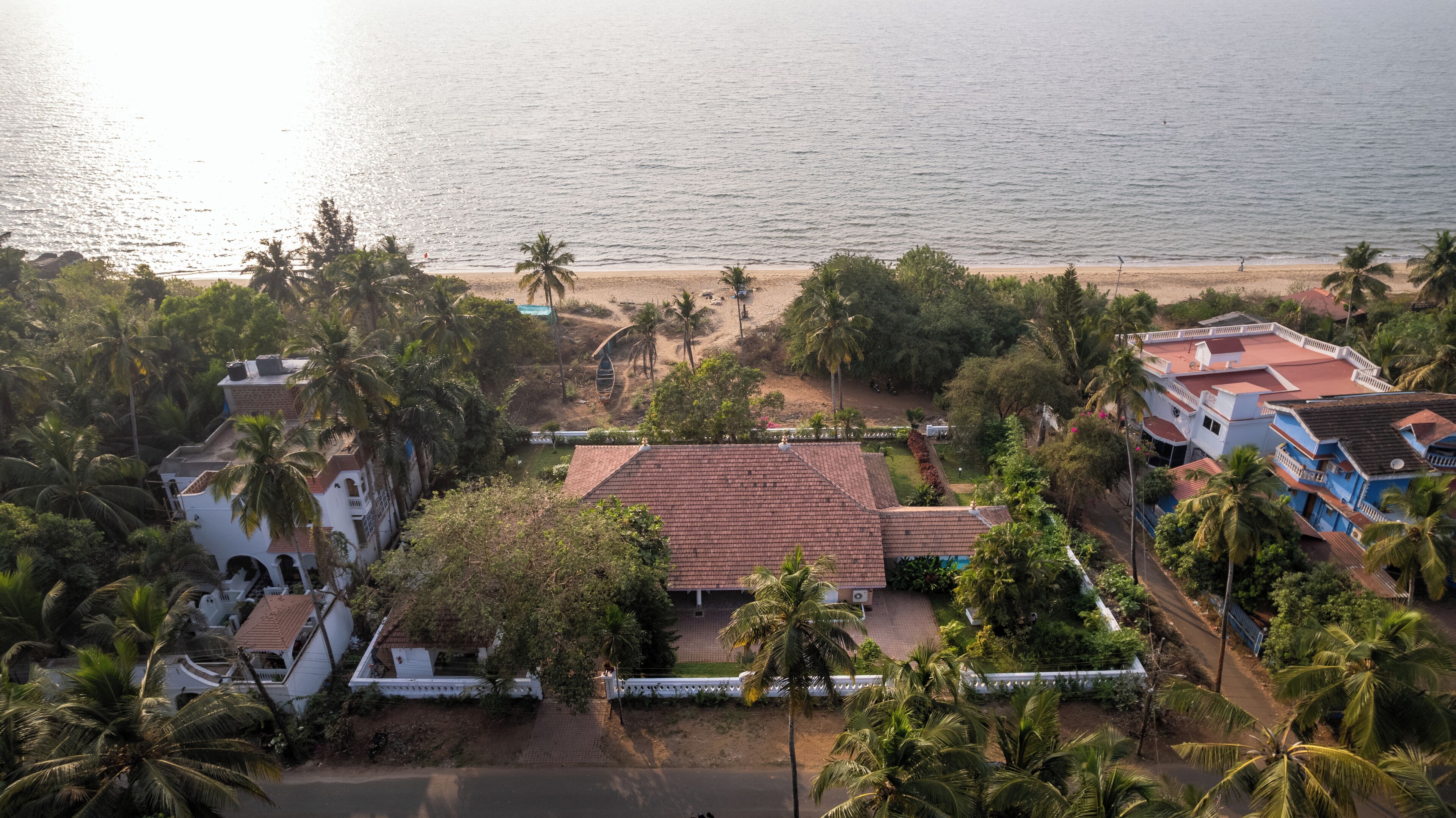 Vista aérea de una zona residencial costera con casas, palmeras y una playa.