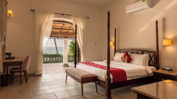 A bedroom with a four-poster bed, a desk, and a view of the sea. - Rosastays Panjim Goa (Panaji)