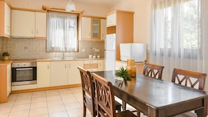 A kitchen with wooden cabinets, a dining table with chairs, a built-in oven, and a window with curtains. - Ilios Kefalonia With 3 Bedrooms and 3 Bathrooms (Kefalonia)