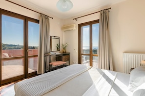 A bedroom with a large bed, a desk, and a view of the city through floor-to-ceiling windows. - Ilios Kefalonia With 3 Bedrooms and 3 Bathrooms (Kefalonia)