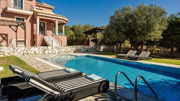 A swimming pool with lounge chairs, a stone wall, and a large tree. - Ilios Kefalonia With 3 Bedrooms and 3 Bathrooms (Kefalonia)