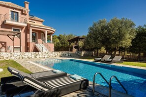 A swimming pool with lounge chairs, a stone wall, and a large tree. - Ilios Kefalonia With 3 Bedrooms and 3 Bathrooms (Kefalonia)