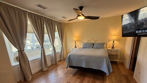 Een slaapkamer met een bed, twee nachtkastjes met lampen, een plafondventilator en een aan de muur bevestigde televisie.