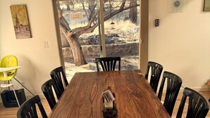 Een eethoek met een houten tafel, zwarte stoelen en zicht op een besneeerd landschap door grote glazen deuren.